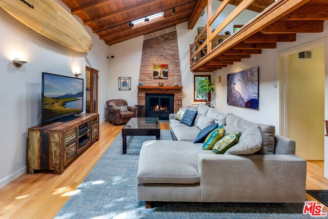 living room featuring wood-type flooring, a skylight, a brick fireplace, wooden ceiling, and beam ceiling