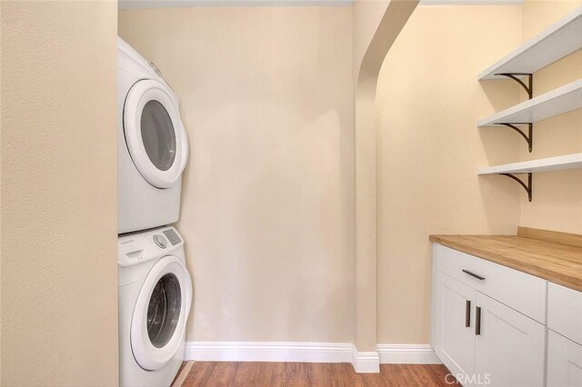 washroom with light hardwood / wood-style floors, cabinets, and stacked washing maching and dryer