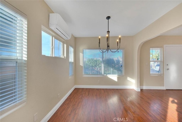 unfurnished dining area with wood-type flooring, a notable chandelier, and a wall mounted air conditioner