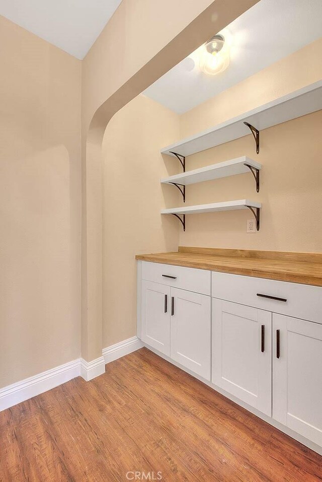 bar featuring butcher block counters, light hardwood / wood-style flooring, and white cabinets