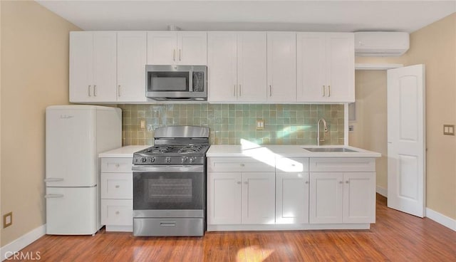 kitchen with a wall mounted AC, stainless steel appliances, decorative backsplash, white cabinets, and sink