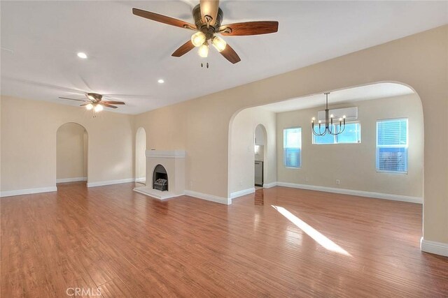 unfurnished living room featuring ceiling fan with notable chandelier and light hardwood / wood-style flooring