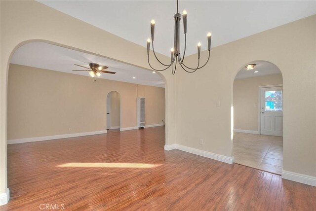 empty room featuring ceiling fan with notable chandelier and hardwood / wood-style flooring