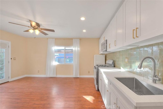 kitchen with appliances with stainless steel finishes, white cabinetry, tasteful backsplash, light hardwood / wood-style floors, and sink