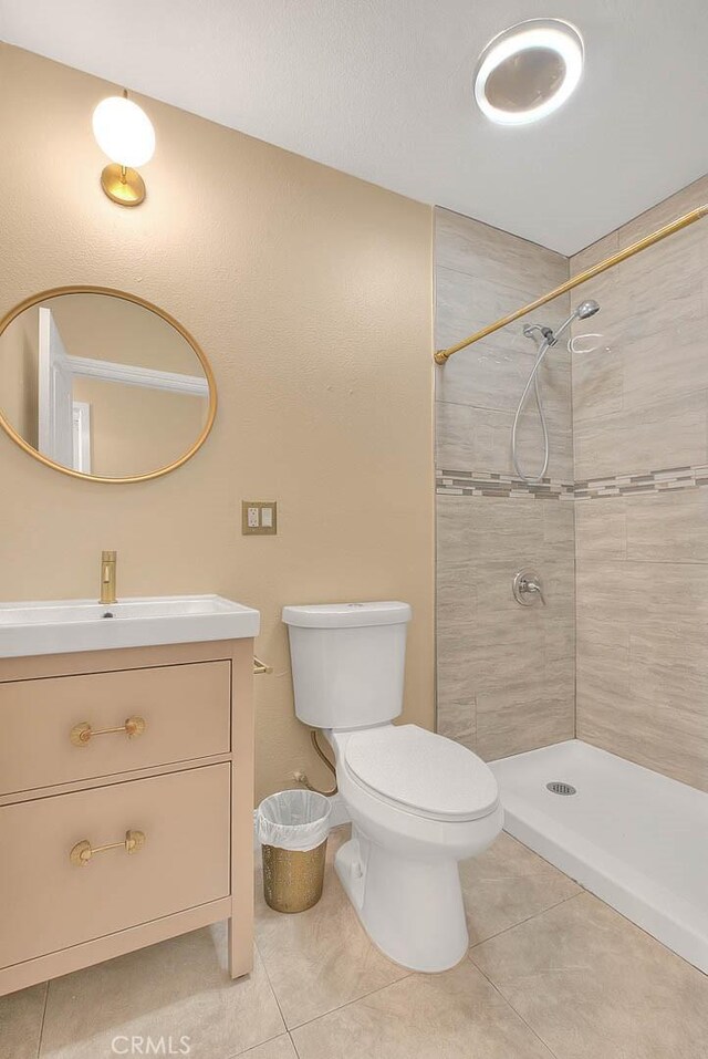 bathroom with toilet, vanity, tile patterned floors, and a tile shower