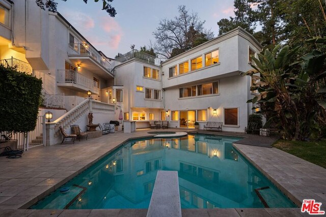 back house at dusk featuring a pool with hot tub and a patio area