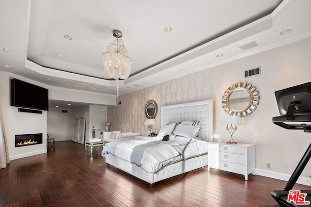 bedroom featuring a tray ceiling, dark hardwood / wood-style flooring, crown molding, and a chandelier