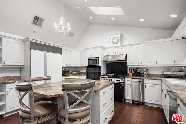 kitchen featuring pendant lighting, white cabinets, a skylight, and built in appliances