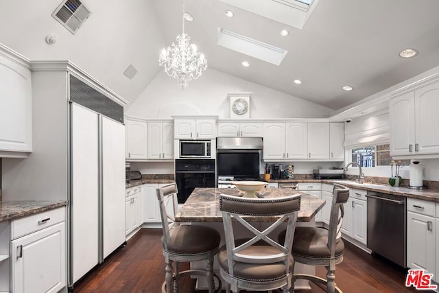 kitchen featuring lofted ceiling with skylight, stone counters, a center island, built in appliances, and white cabinets