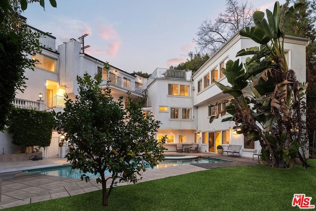 pool at dusk featuring a lawn and a patio