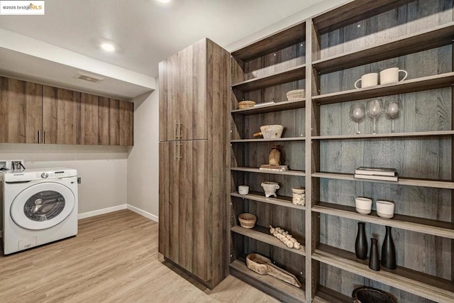 clothes washing area featuring washer / dryer, cabinets, and light hardwood / wood-style flooring