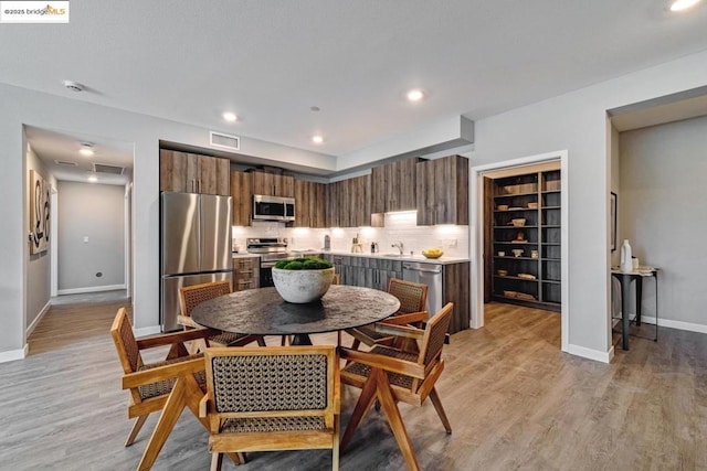 interior space featuring light wood-type flooring, stainless steel appliances, dark brown cabinets, and backsplash