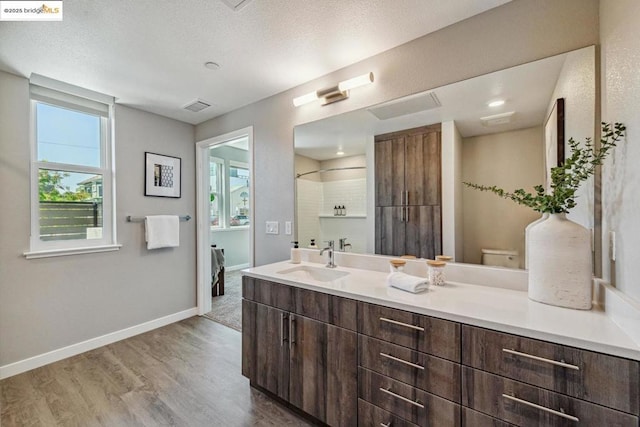 bathroom with a textured ceiling, wood-type flooring, vanity, a shower, and toilet