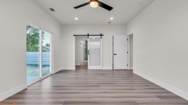 unfurnished bedroom featuring ceiling fan, access to exterior, light hardwood / wood-style flooring, and a barn door