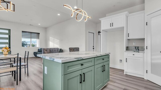 kitchen featuring decorative light fixtures, green cabinets, white cabinetry, light wood-type flooring, and light stone counters