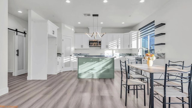 kitchen with white cabinets, a center island, decorative light fixtures, light hardwood / wood-style flooring, and a barn door