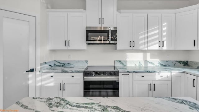 kitchen with appliances with stainless steel finishes, white cabinetry, and light stone counters