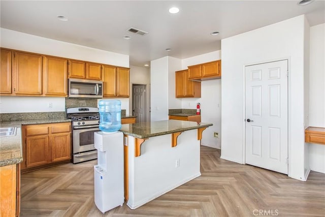 kitchen with a center island, a kitchen bar, stainless steel appliances, dark stone countertops, and light parquet floors