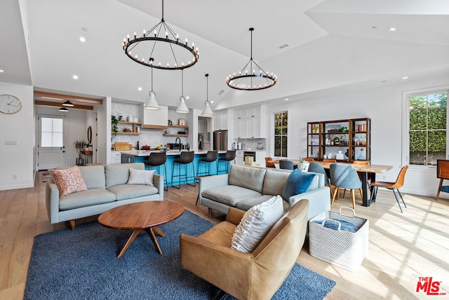 living room with lofted ceiling, light wood-type flooring, sink, and ceiling fan with notable chandelier