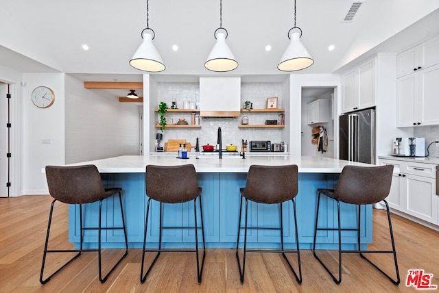 kitchen featuring decorative light fixtures, backsplash, a large island, high end fridge, and a breakfast bar area