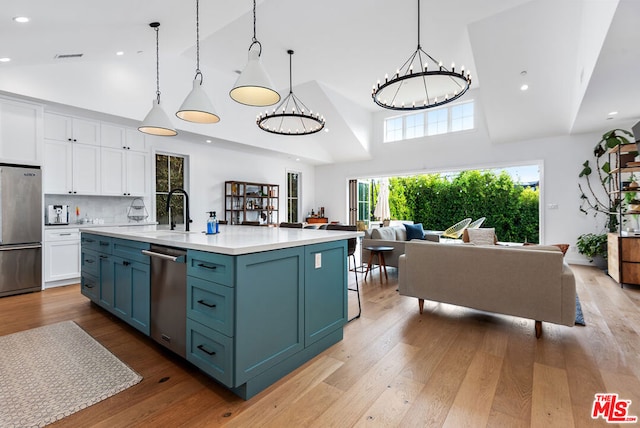 kitchen featuring decorative light fixtures, white cabinetry, stainless steel appliances, an island with sink, and high vaulted ceiling