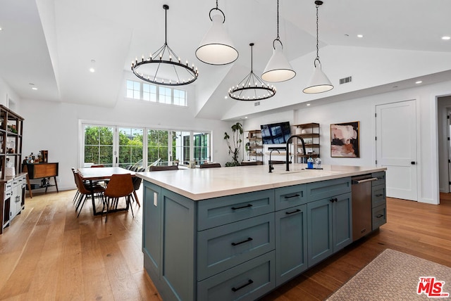 kitchen with a center island with sink, pendant lighting, sink, an inviting chandelier, and light wood-type flooring