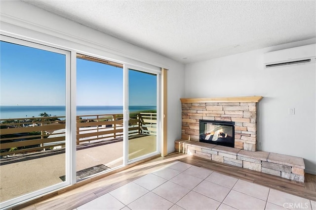 unfurnished living room with a wall mounted air conditioner, a textured ceiling, a water view, a fireplace, and light tile patterned flooring