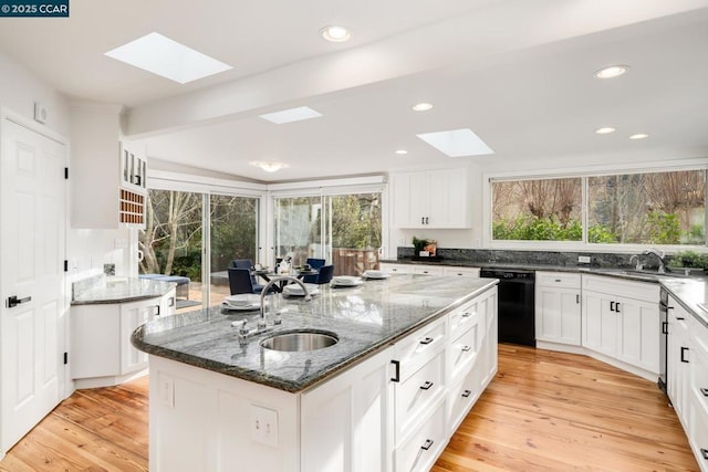 kitchen with a kitchen island with sink, a skylight, sink, and black dishwasher