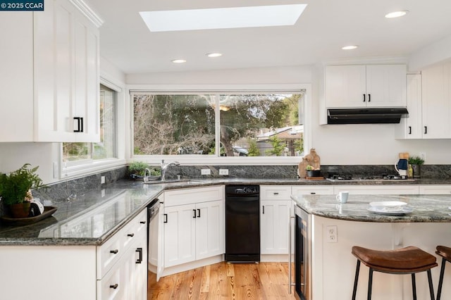 kitchen featuring white cabinets, a skylight, stainless steel appliances, and dark stone countertops