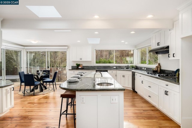 kitchen featuring a skylight, sink, dark stone counters, and an island with sink