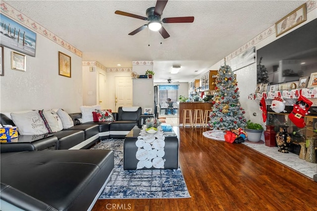 living room with a textured ceiling, ceiling fan, and dark hardwood / wood-style floors