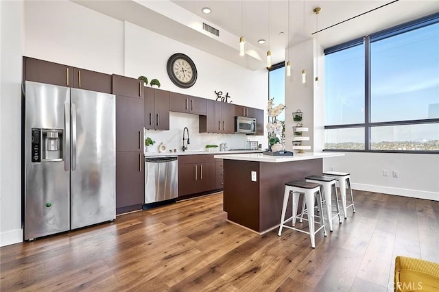 kitchen with appliances with stainless steel finishes, dark hardwood / wood-style floors, a kitchen breakfast bar, dark brown cabinetry, and a center island