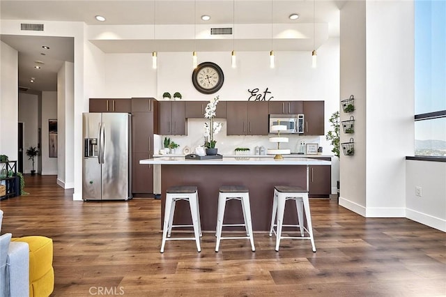 kitchen with decorative light fixtures, a kitchen island, appliances with stainless steel finishes, a kitchen breakfast bar, and dark brown cabinets