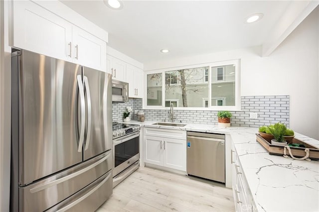 kitchen with sink, white cabinetry, light hardwood / wood-style flooring, light stone countertops, and appliances with stainless steel finishes