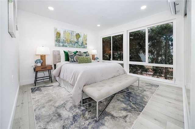 bedroom with a wall mounted AC and light hardwood / wood-style floors