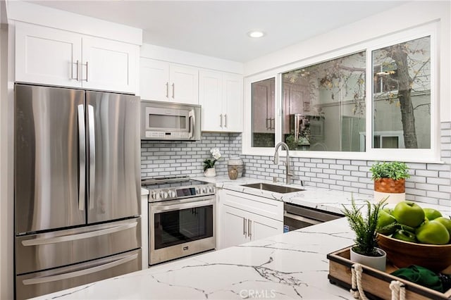 kitchen with stainless steel appliances, backsplash, light stone countertops, white cabinets, and sink