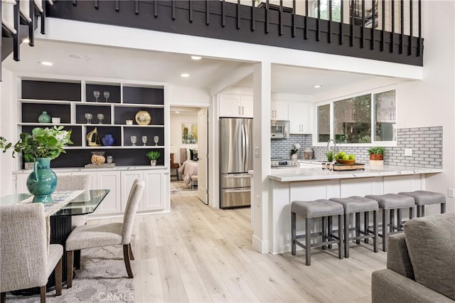 kitchen with white cabinetry, stainless steel appliances, light hardwood / wood-style floors, kitchen peninsula, and a breakfast bar