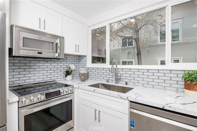 kitchen featuring white cabinetry, stainless steel appliances, sink, backsplash, and light stone counters