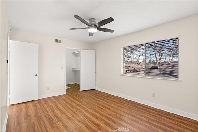 unfurnished bedroom with a spacious closet, a closet, hardwood / wood-style flooring, and ceiling fan