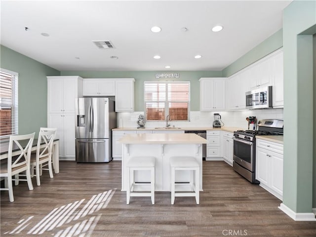 kitchen featuring stainless steel appliances, white cabinetry, a kitchen island, and sink