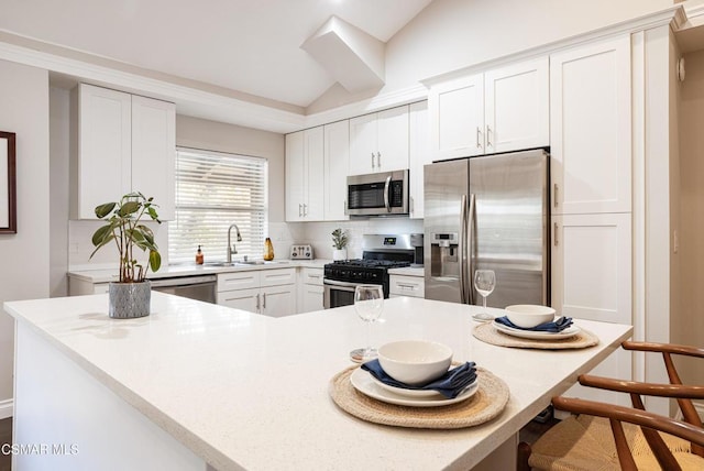 kitchen featuring a kitchen bar, white cabinetry, appliances with stainless steel finishes, and vaulted ceiling