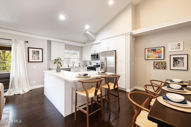 kitchen with white cabinets, appliances with stainless steel finishes, dark wood-type flooring, sink, and a breakfast bar area