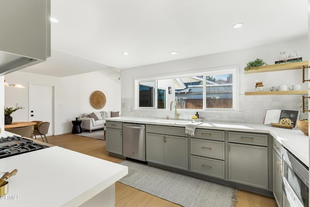 kitchen featuring light hardwood / wood-style floors, gray cabinetry, decorative backsplash, dishwasher, and sink