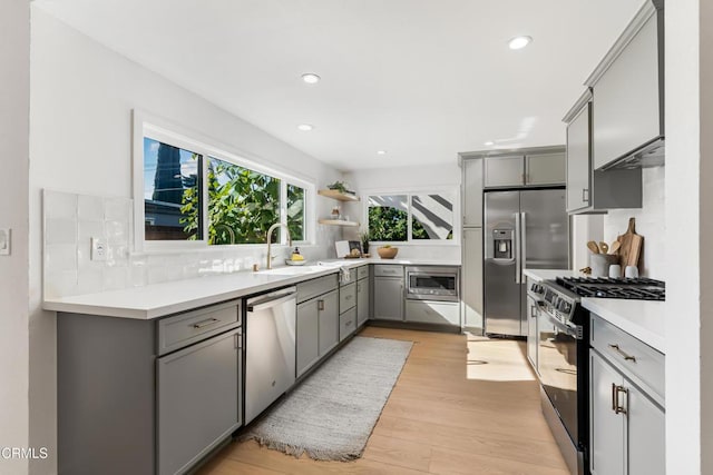 kitchen featuring appliances with stainless steel finishes, gray cabinetry, decorative backsplash, light hardwood / wood-style flooring, and sink