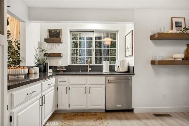 kitchen with stainless steel dishwasher, sink, white cabinets, and light wood-type flooring