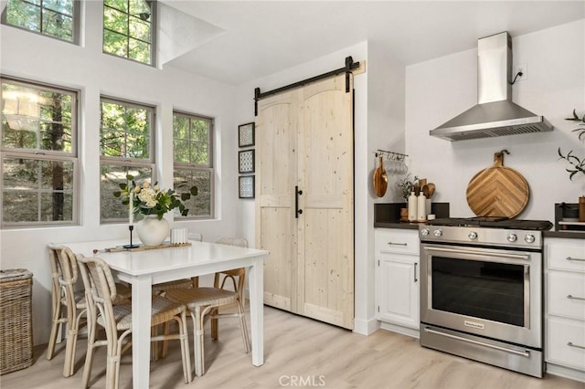 kitchen with a barn door, exhaust hood, stainless steel stove, light hardwood / wood-style flooring, and white cabinets