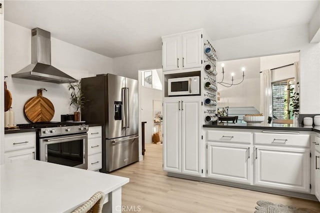 kitchen featuring appliances with stainless steel finishes, light hardwood / wood-style floors, white cabinets, and wall chimney range hood