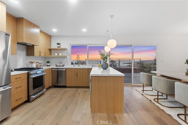 kitchen with decorative light fixtures, a center island, light hardwood / wood-style floors, sink, and appliances with stainless steel finishes