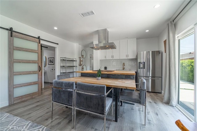 kitchen featuring wood counters, white cabinetry, wall chimney range hood, stainless steel fridge, and a barn door