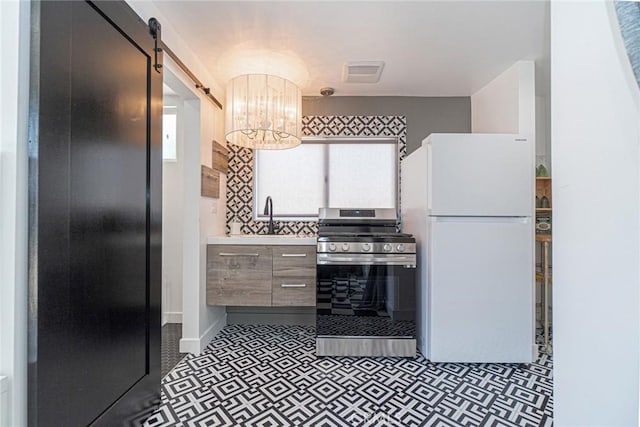 kitchen featuring dark tile patterned flooring, stainless steel range oven, white fridge, a chandelier, and a barn door